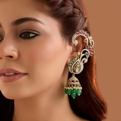 Gold plated peacock design jhumka earrings with American diamond stones, ruby pink accents and green bead and pearl hangings on a white background