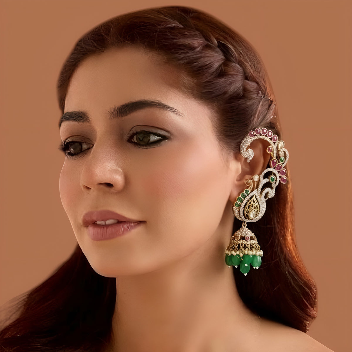Gold plated peacock design jhumka earrings with American diamond stones, ruby pink accents and green bead and pearl hangings on a white background