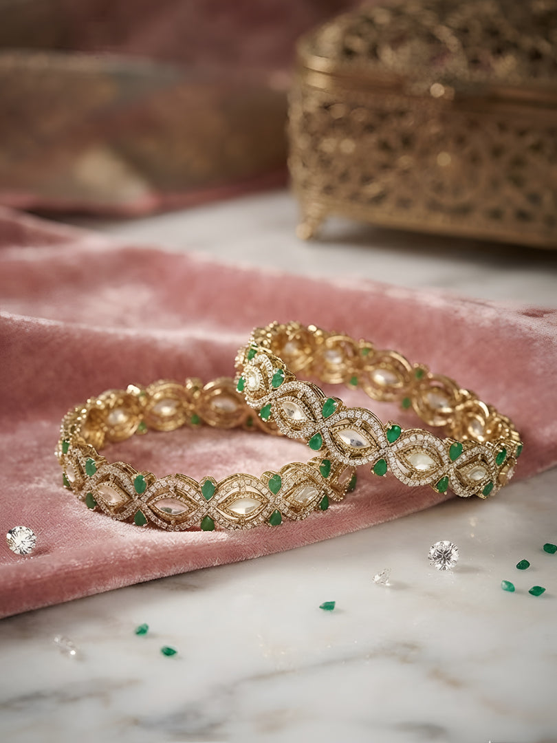 "Pair of gold-plated Kundan bangles with emerald green stones, traditional Indian bridal jewelry on pink velvet background"