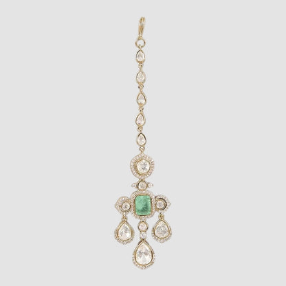 Gold-plated kundan maang tikka with emerald center and pear-shaped stones on a neutral background