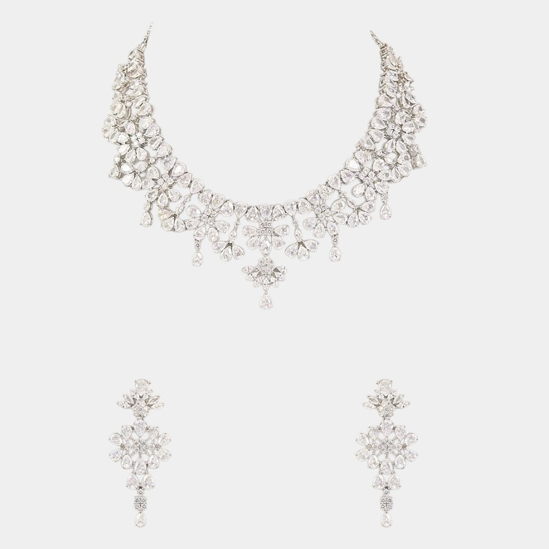 “Silver-tone crystal necklace with matching dangling earrings featuring floral and teardrop stone design.”