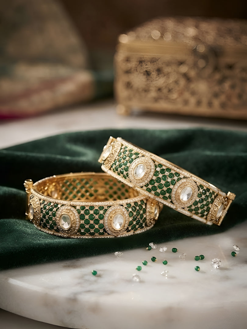 "Pair of gold-plated bangles with emerald green pave stones and Kundan detailing, traditional Indian jewelry