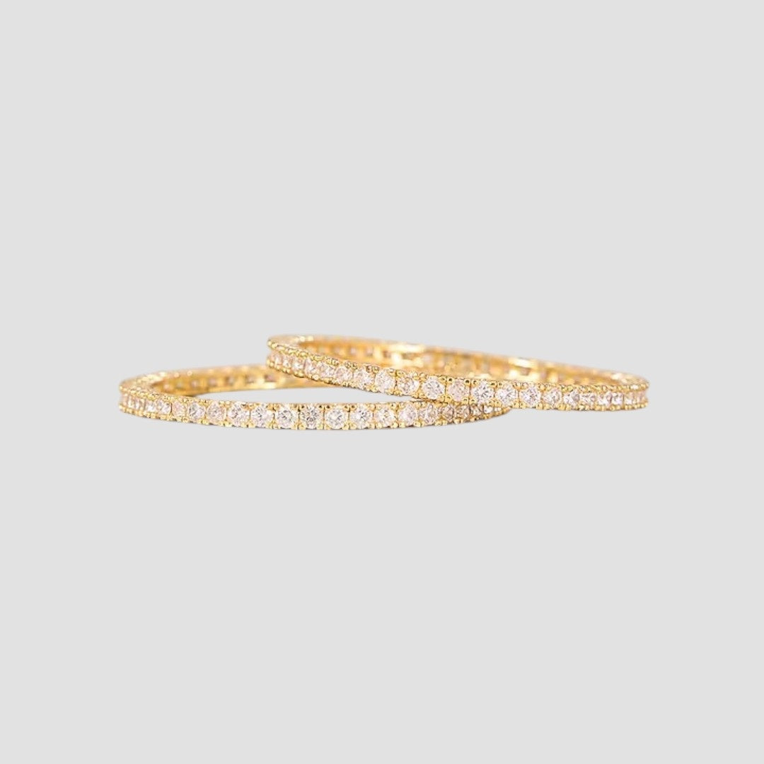Gold-plated slim bangles set studded with sparkling stones on a light background