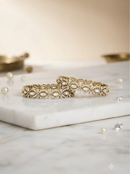 Pair of gold-toned floral bangles with white stone embellishments on a neutral background