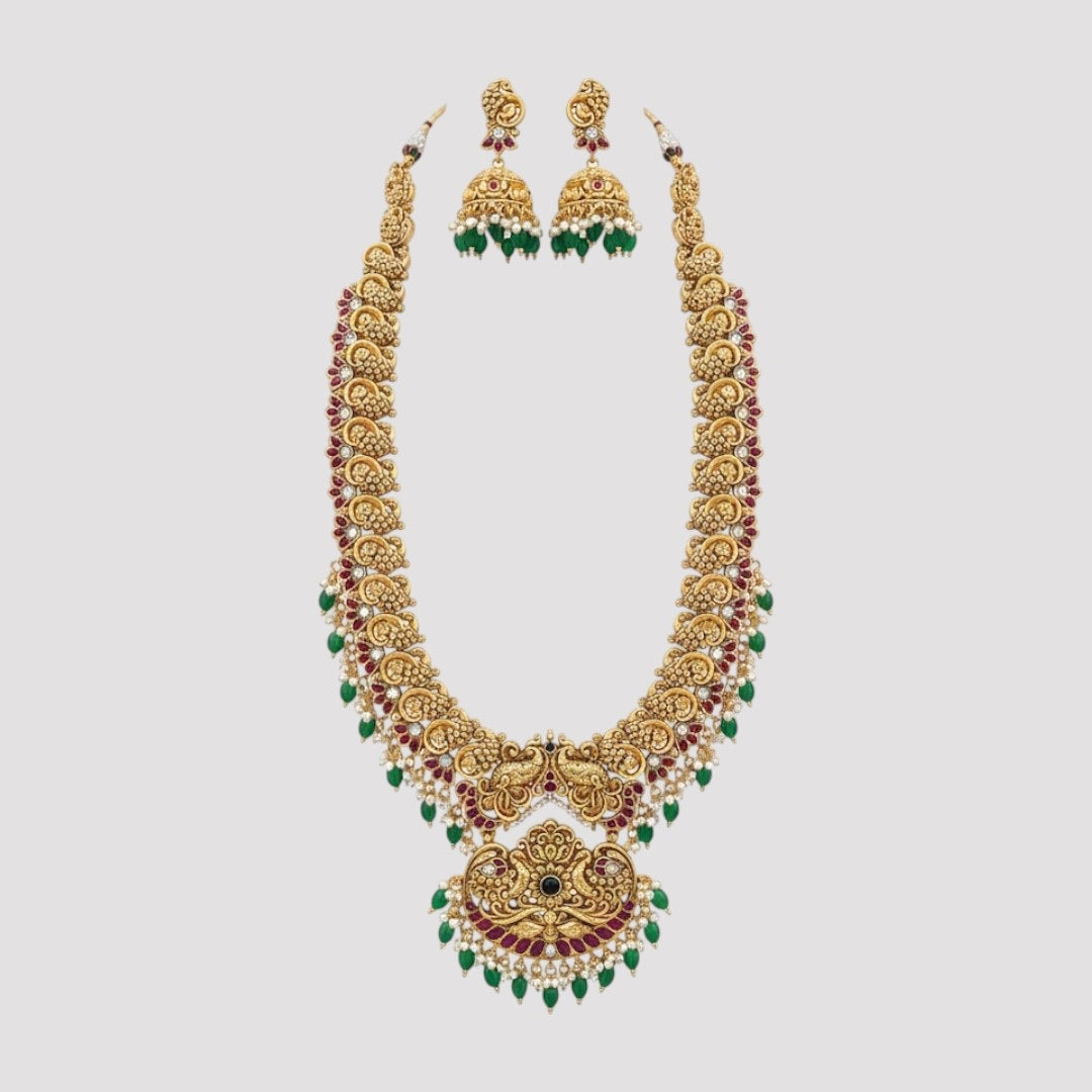“Antique gold-plated temple necklace set with Lakshmi design, ruby stones, green beads, and matching jhumka earrings.”