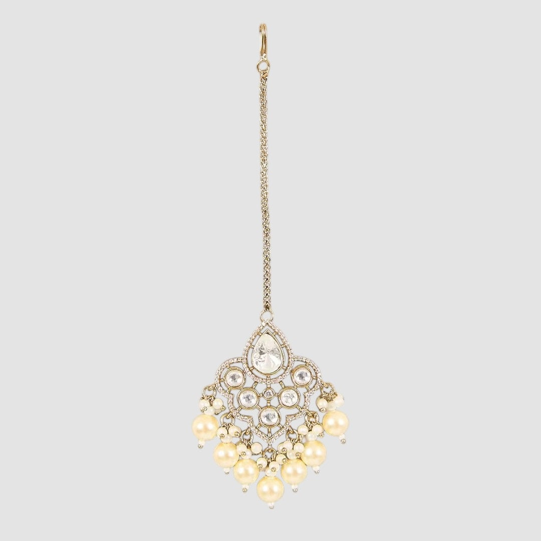 Gold-plated maang tikka with kundan stones and cream pearl danglers on a light background