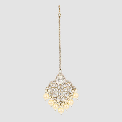Gold-plated maang tikka with kundan stones and cream pearl danglers on a light background