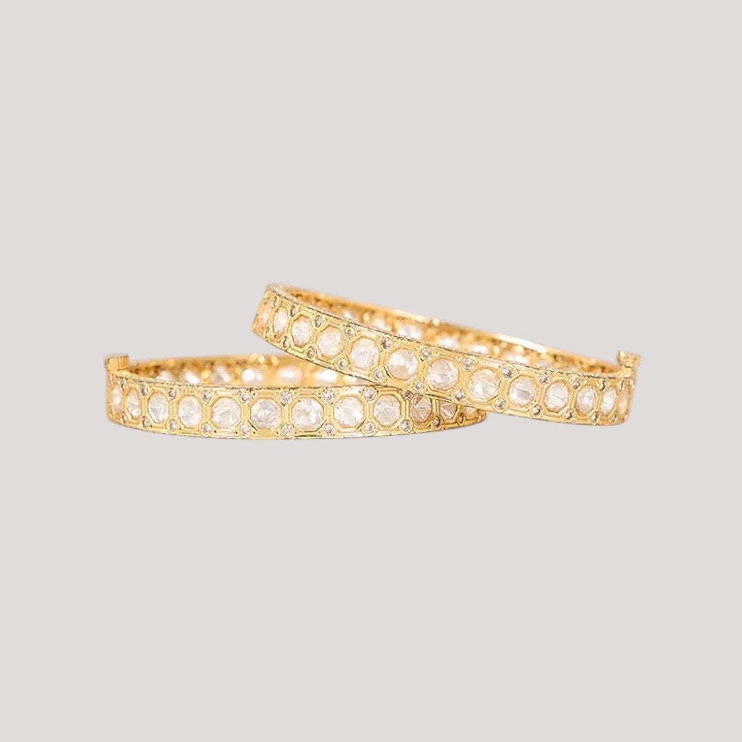 “Pair of gold-plated bangles with circular stone-studded design on a neutral background.”