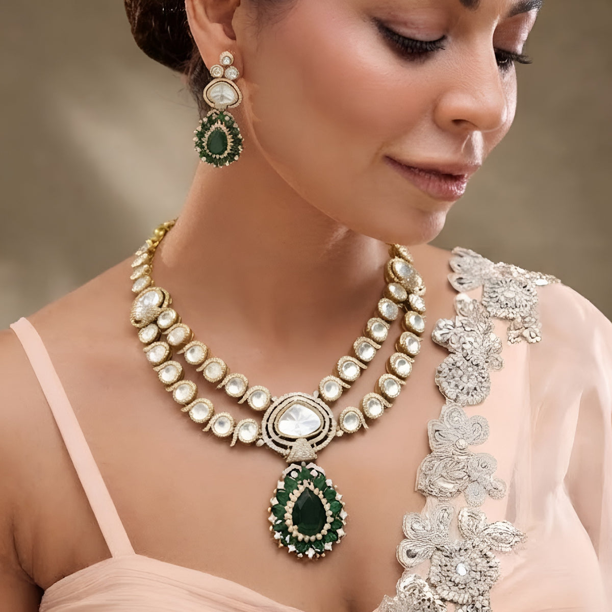 Antique gold two-strand polki kundan necklace with emerald green teardrop pendant on a display bust