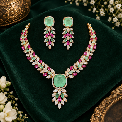 Rose gold American diamond leaf-vine necklace set with a mint-green square centre stone, ruby-pink accents and matching leaf-drop earrings on a grey display bust