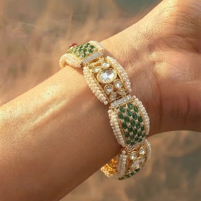 "Gold-tone bridal bracelet with pearl, emerald green, and white kundan stone panels and ruby drop clasp"