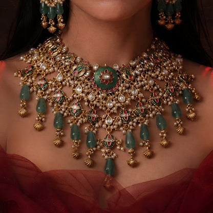 "Antique gold Kundan choker necklace and earring set with green floral meenakari centerpiece and emerald bead drops, traditional jewellery on maroon backdrop"
