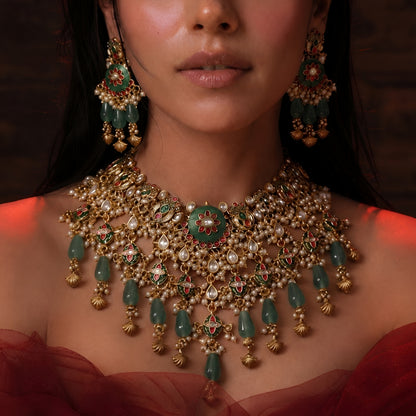 "Antique gold Kundan choker necklace and earring set with green floral meenakari centerpiece and emerald bead drops, traditional jewellery on maroon backdrop"