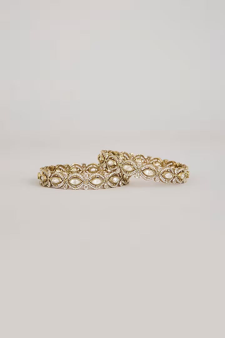 Pair of gold-toned floral bangles with white stone embellishments on a neutral background