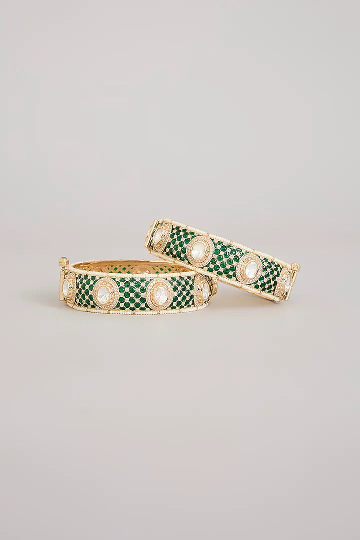 "Pair of gold-plated bangles with emerald green pave stones and Kundan detailing, traditional Indian jewelry