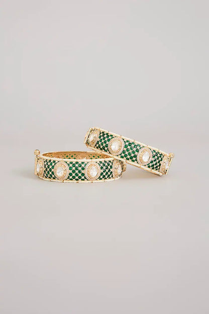 "Pair of gold-plated bangles with emerald green pave stones and Kundan detailing, traditional Indian jewelry