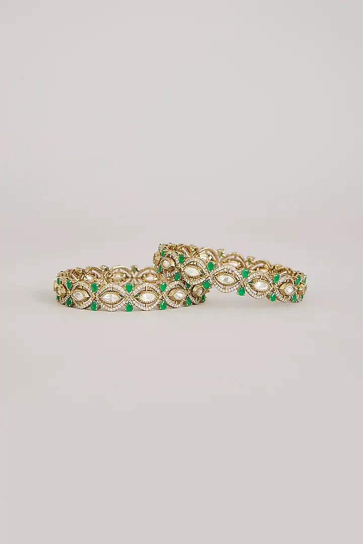 "Pair of gold-plated Kundan bangles with emerald green stones, traditional Indian bridal jewelry on pink velvet background"