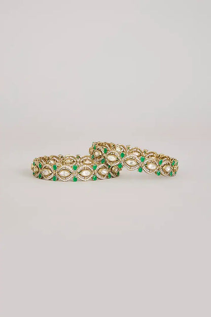 "Pair of gold-plated Kundan bangles with emerald green stones, traditional Indian bridal jewelry on pink velvet background"