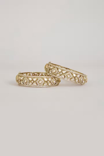 "Pair of gold-plated Kundan bangles with white stones in floral geometric design, traditional Indian bridal jewelry on white background"