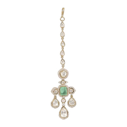 Gold-plated kundan maang tikka with emerald center and pear-shaped stones on a neutral background
