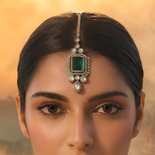 Gold maang tikka with emerald cut green stone in kundan halo setting and pearl chain, Indian bridal hair jewelry on white background