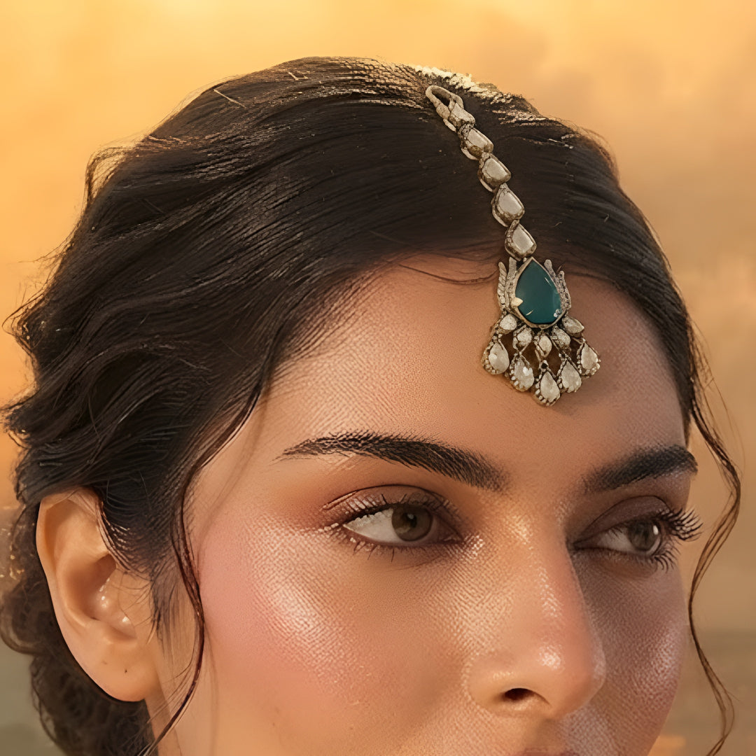 Gold maang tikka with pear-cut emerald green stone and clear kundan crystal chain, Indian bridal hair jewelry on white background