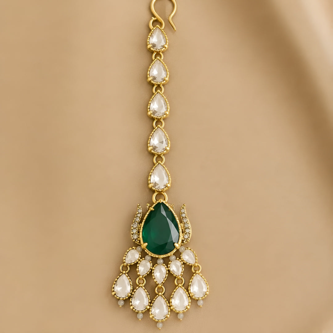 Gold maang tikka with pear-cut emerald green stone and clear kundan crystal chain, Indian bridal hair jewelry on white background