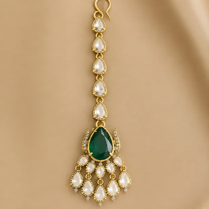 Gold maang tikka with pear-cut emerald green stone and clear kundan crystal chain, Indian bridal hair jewelry on white background