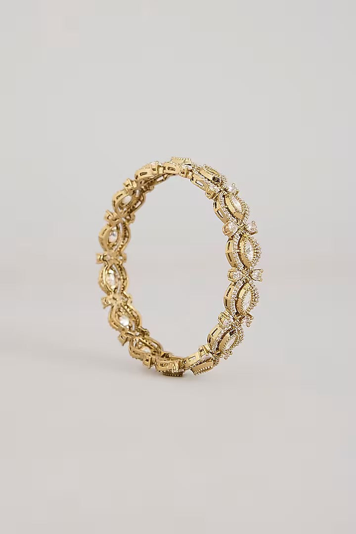 Pair of gold-toned floral bangles with white stone embellishments on a neutral background
