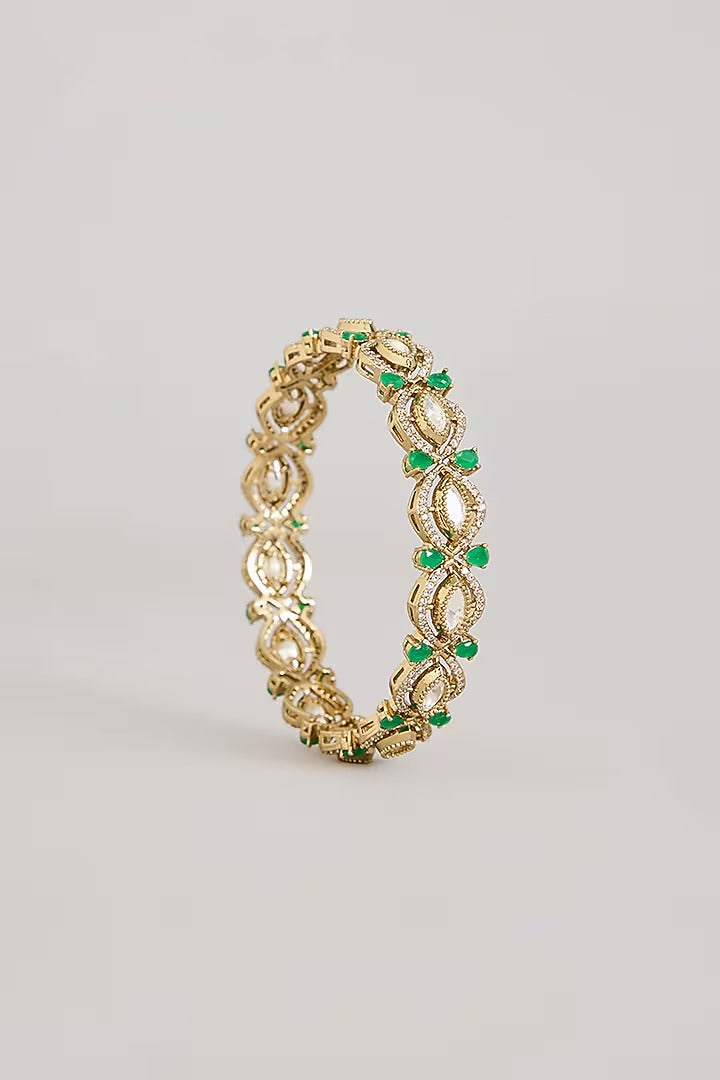 "Pair of gold-plated Kundan bangles with emerald green stones, traditional Indian bridal jewelry on pink velvet background"