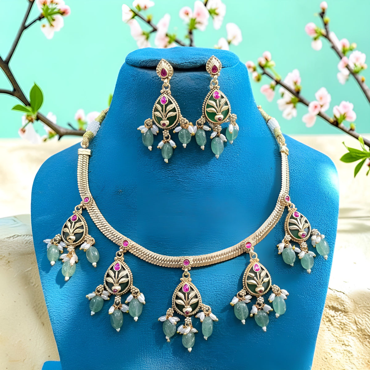 Antique gold plated necklace set with dark green pear medallions, pink stones, mint green bead and pearl drops and matching earrings on a blue bust
