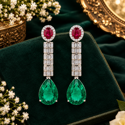 Silver-tone American diamond long drop earrings with ruby-red oval top stones, clear baguette stone rows and large emerald-green pear-cut drops on dark green velvet