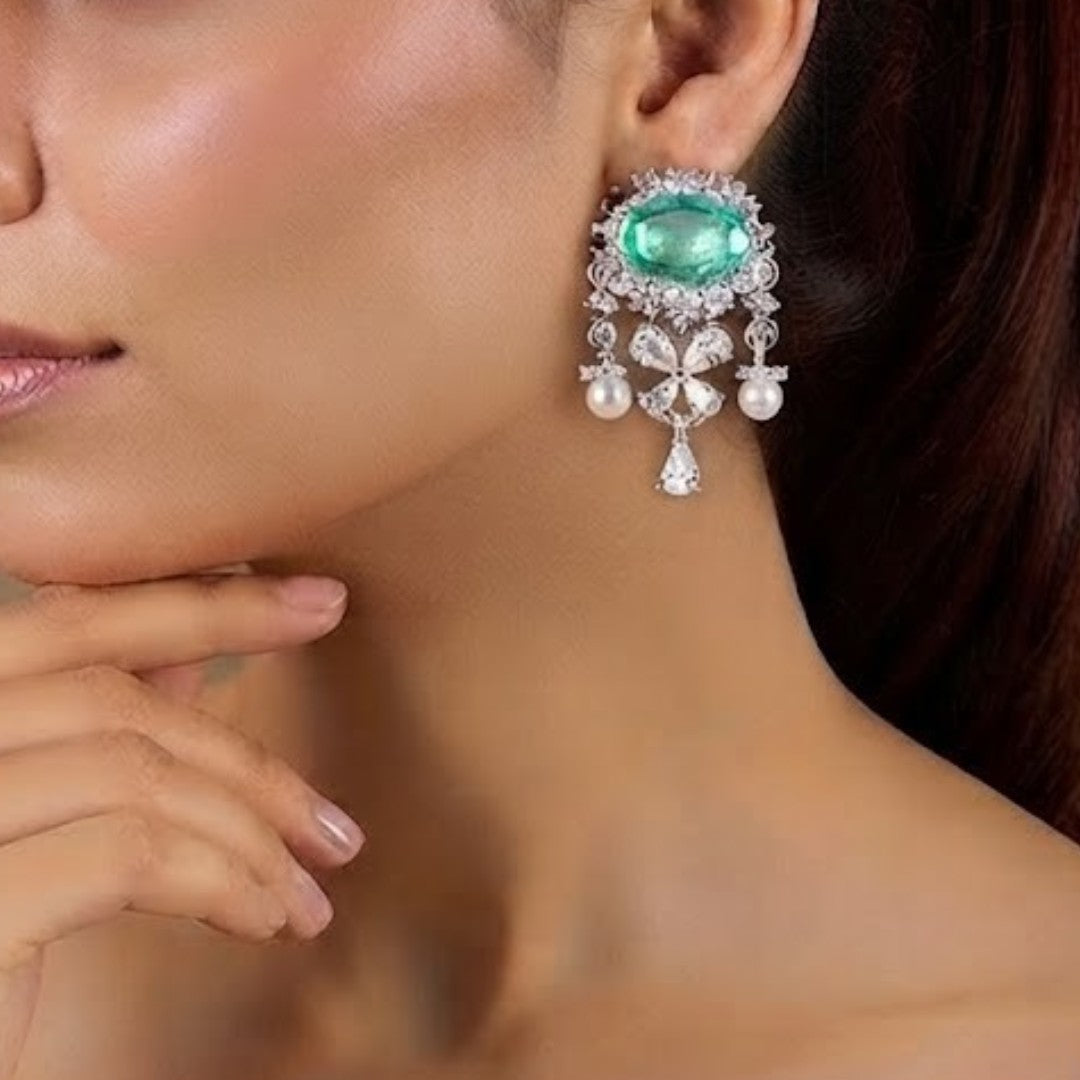 "Silver rhodium-plated drop earrings with oval emerald stone, diamond halo, clover-shaped white stones and pearl bead accents"
