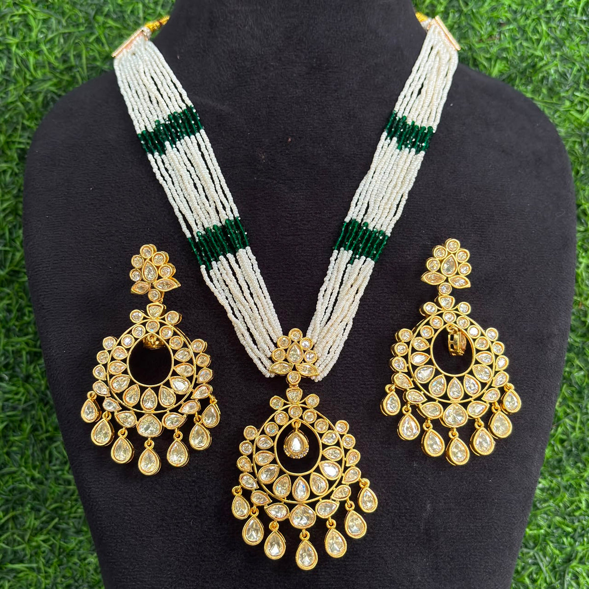 Multi-strand white pearl necklace with green bead bands and gold kundan chandbali pendant on a display bust