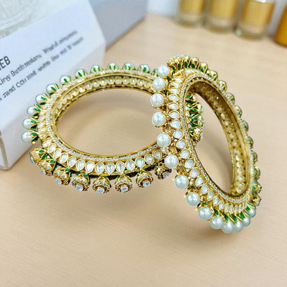 Gold - Plated Pearl & Kundan Bangles with Green Enamel Detailing - Auraa Trends - Bangles -  - Auraa Trends - Gold - plated bangles with kundan stones, pearl embellishments, and jhumka - style hanging drops, displayed on dark green velvet background