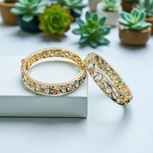 Gold - Toned Kundan Filigree Bangles with Teardrop Stones - Auraa Trends - Bangles -  - Auraa Trends - “Pair of gold - tone bangles with filigree cutwork and teardrop kundan stones, displayed on dark green velvet