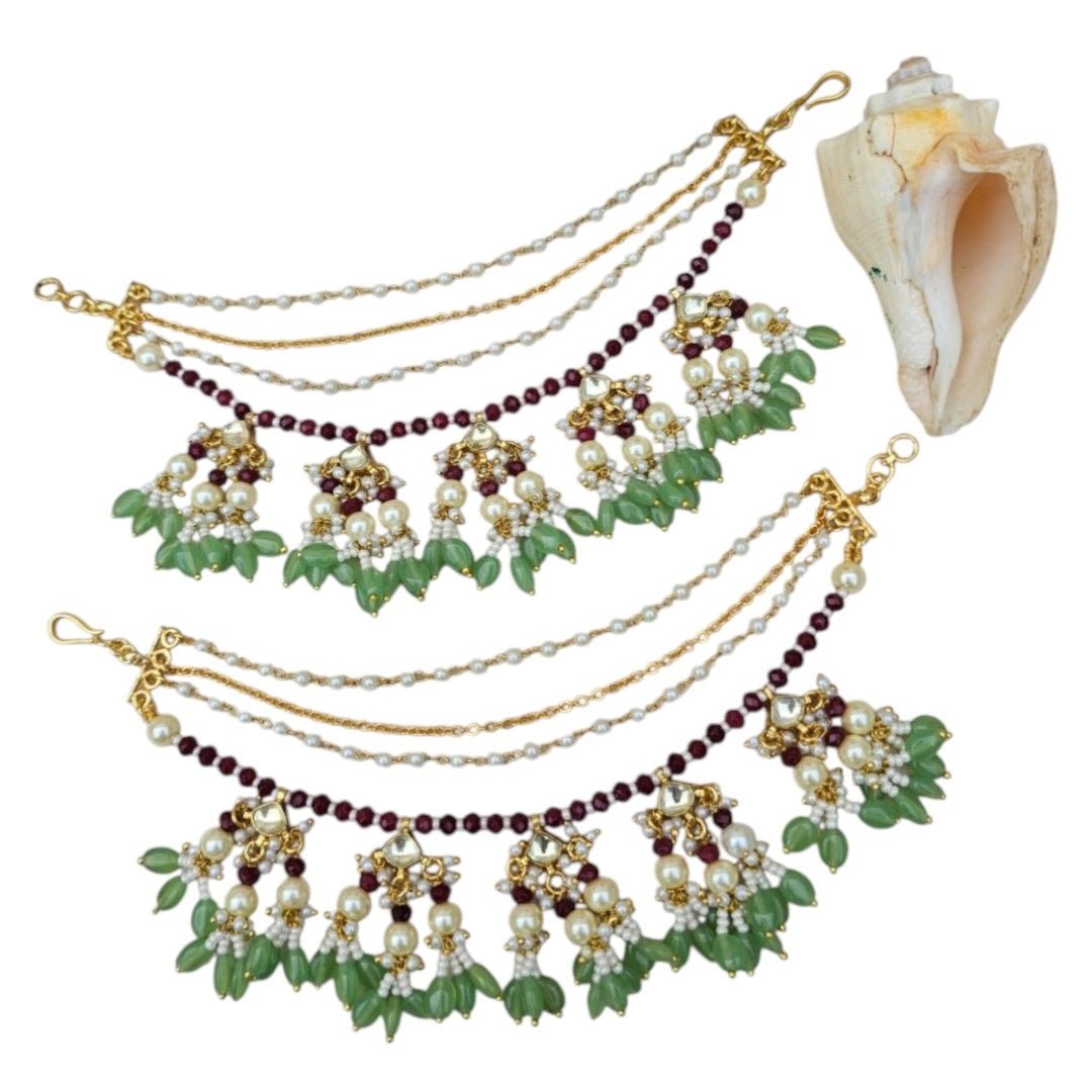 Green & Maroon Kundan Pearl Multi - Layer Kaan Chain - Auraa Trends - Kaan chain -  - Auraa Trends - Traditional multi - layer Kundan Pearl Kaan Chain with maroon beads, green drop beads, floral motifs, and pearl clusters, displayed on a soft fabric background with decorative flowers and a seashell.
