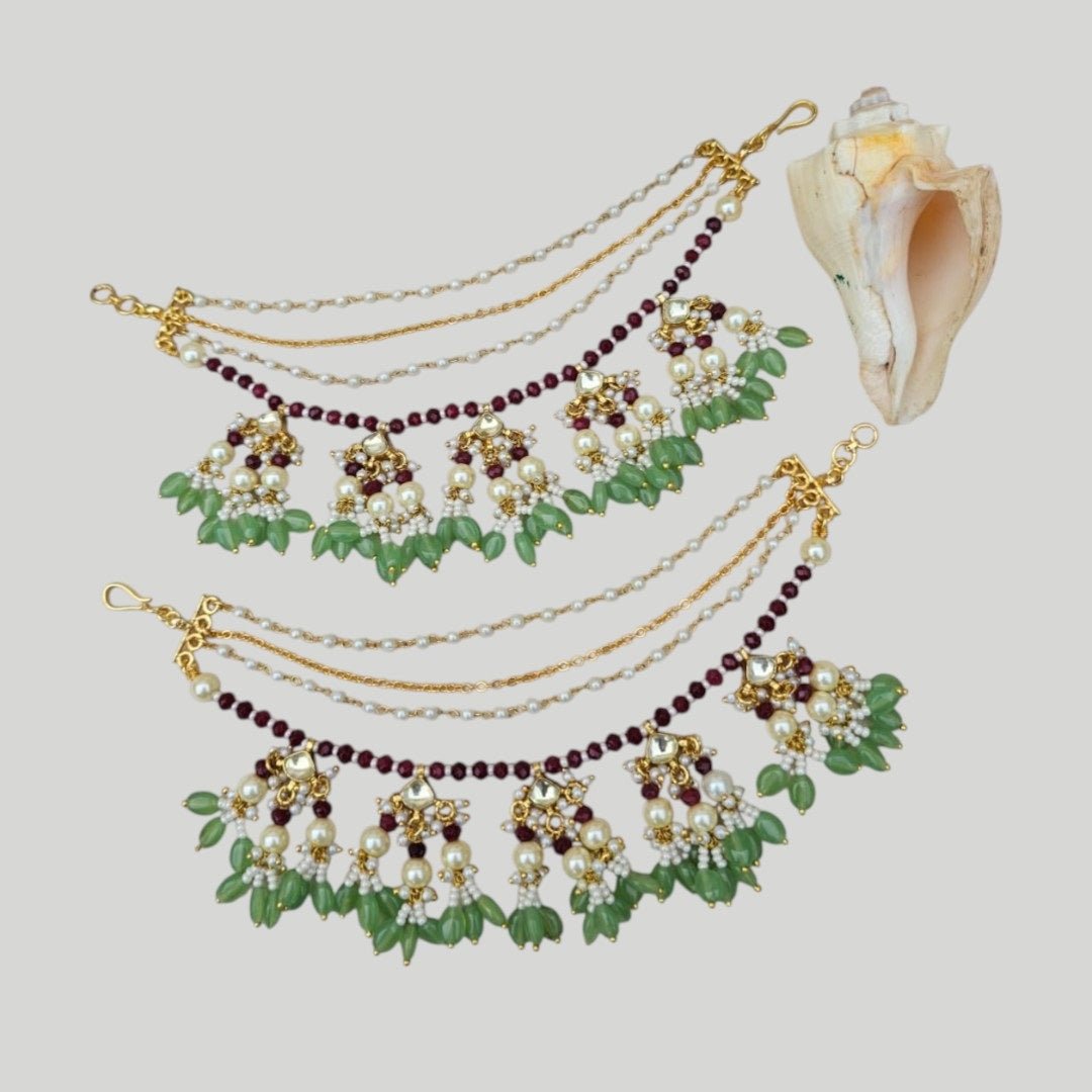 Green & Maroon Kundan Pearl Multi - Layer Kaan Chain - Auraa Trends - Kaan chain -  - Auraa Trends - Traditional multi - layer Kundan Pearl Kaan Chain with maroon beads, green drop beads, floral motifs, and pearl clusters, displayed on a soft fabric background with decorative flowers and a seashell.