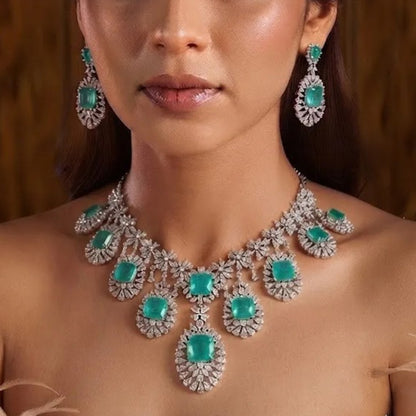 "Silver rhodium-plated multi-tier bridal necklace set with white American diamonds and cushion-cut emerald green stones, paired with matching drop earrings"