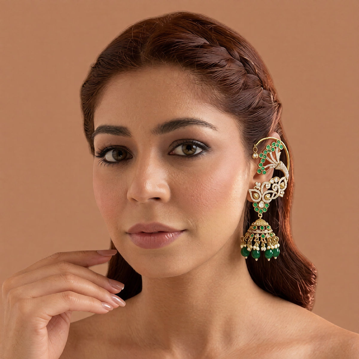 Gold plated emerald green ear cuff jhumka earrings with American diamond stones, green beads and pearl hangings on a white background