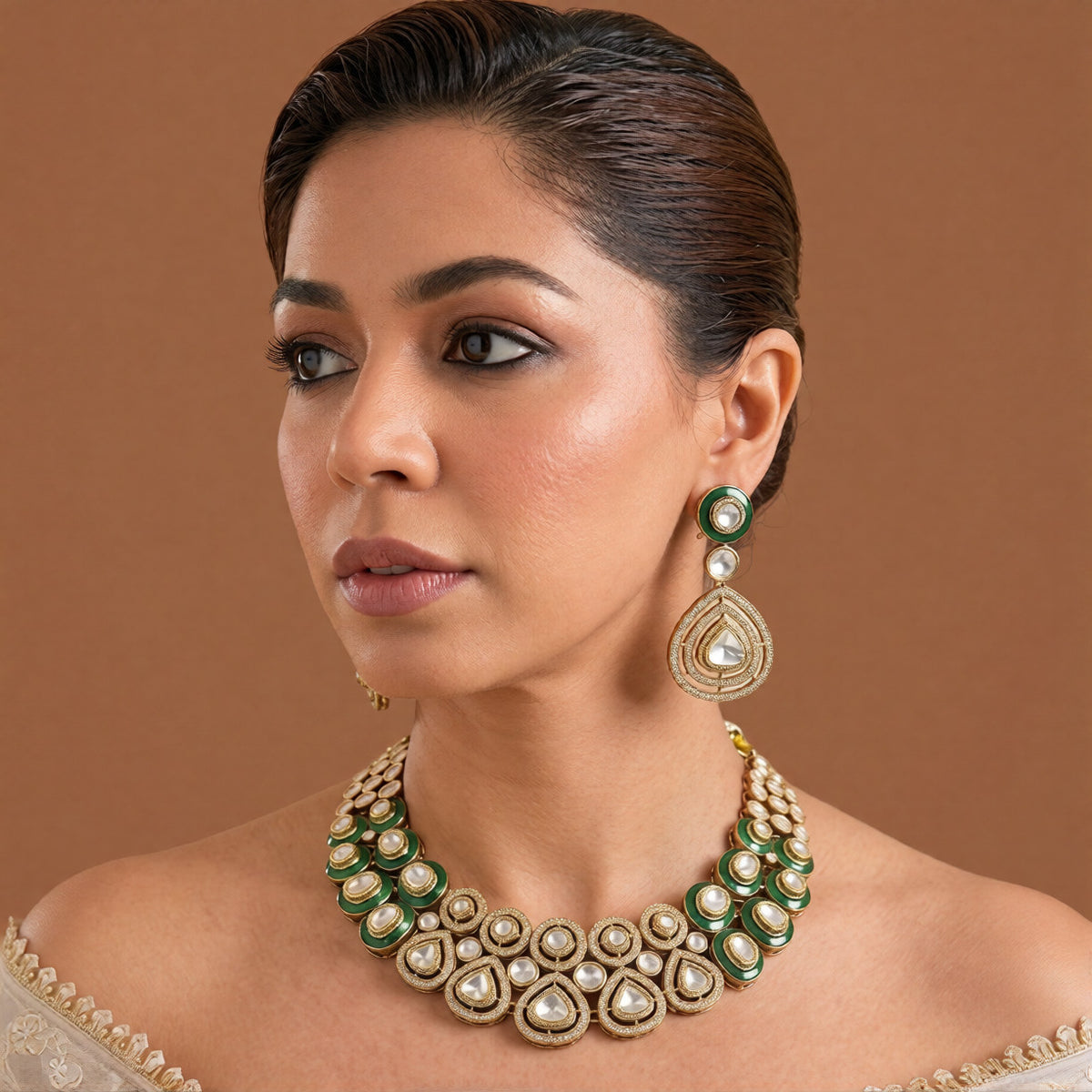Gold-tone emerald green kundan choker necklace set with zircon halo medallions, pear-shaped clear stones and matching pear drop earrings on dark green velvet