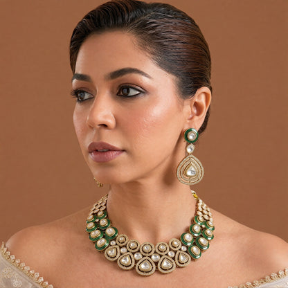 Gold-tone emerald green kundan choker necklace set with zircon halo medallions, pear-shaped clear stones and matching pear drop earrings on dark green velvet
