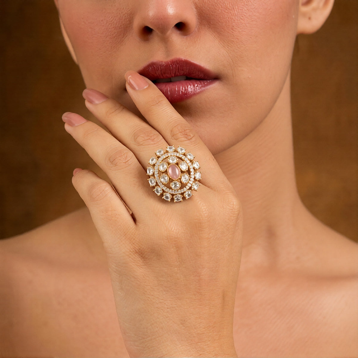 Gold-finish round cocktail ring with a blush-pink oval centre stone, clear oval stones, and American diamond halo