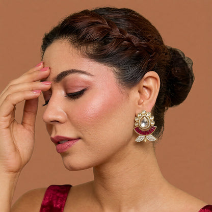 Pair of gold kundan-style stud earrings with a clear pear centre stone, ruby-pink baguette fan and zircon leaf base on a marble slab