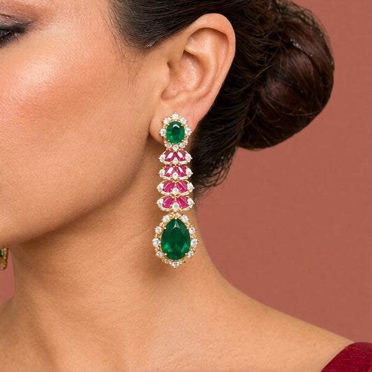Gold-tone American diamond long drop earrings with emerald-green oval tops, ruby-pink marquise leaf rows and large emerald-green pear drops on dark green velvet