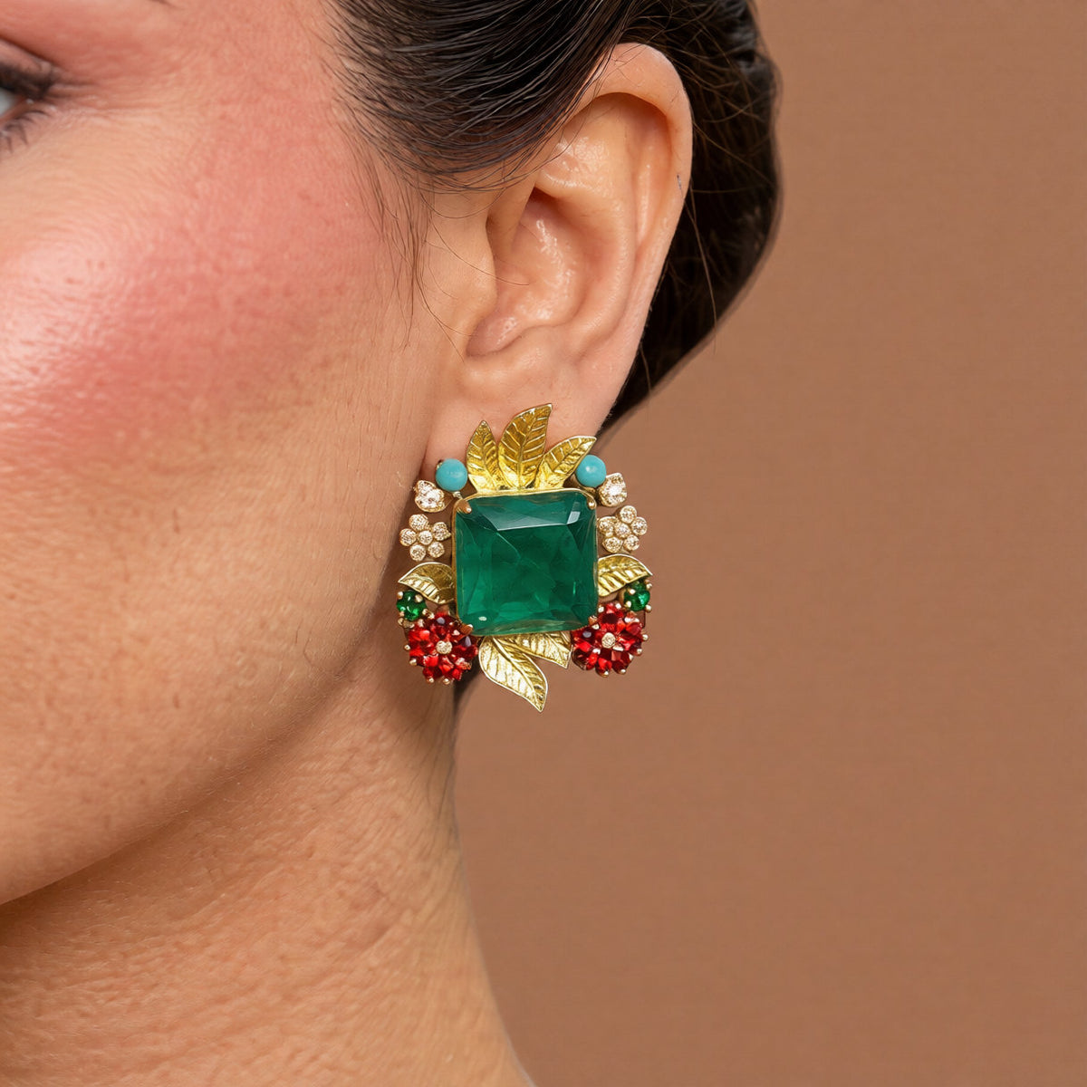 Pair of gold stud earrings with emerald-cut green centre stones, gold leaves, ruby-pink stone clusters, turquoise beads and pearls on a white background