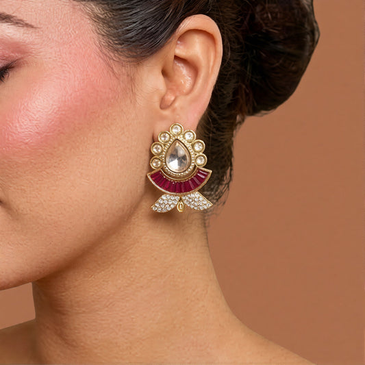 Pair of gold kundan-style stud earrings with a clear pear centre stone, ruby-pink baguette fan and zircon leaf base on a marble slab