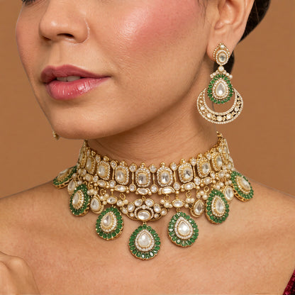Gold Victorian kundan bridal choker with emerald-green ringed pear drops and matching crescent chandelier earrings on dark green velvet