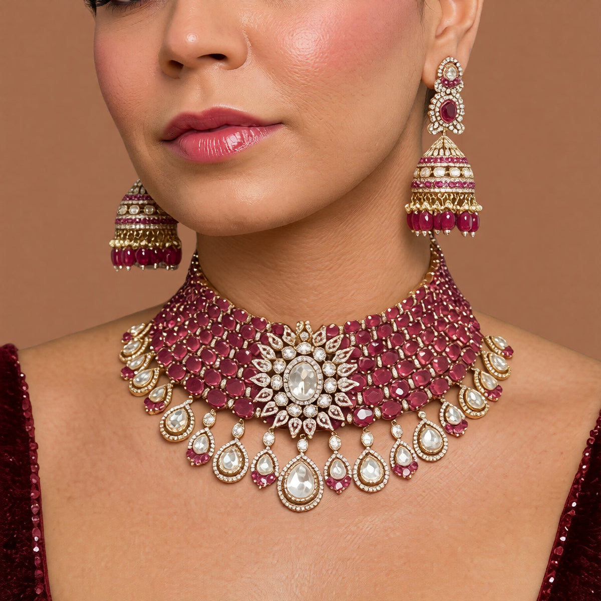 Antique gold Victorian bridal choker set with ruby-red oval stones, kundan floral centre and pear drops with matching ruby jhumka earrings on a white background
