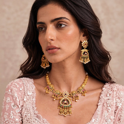 Antique matte gold temple necklace set with green triangular pendant, ruby pink stones, pearl drops and matching chandelier earrings on teal bust